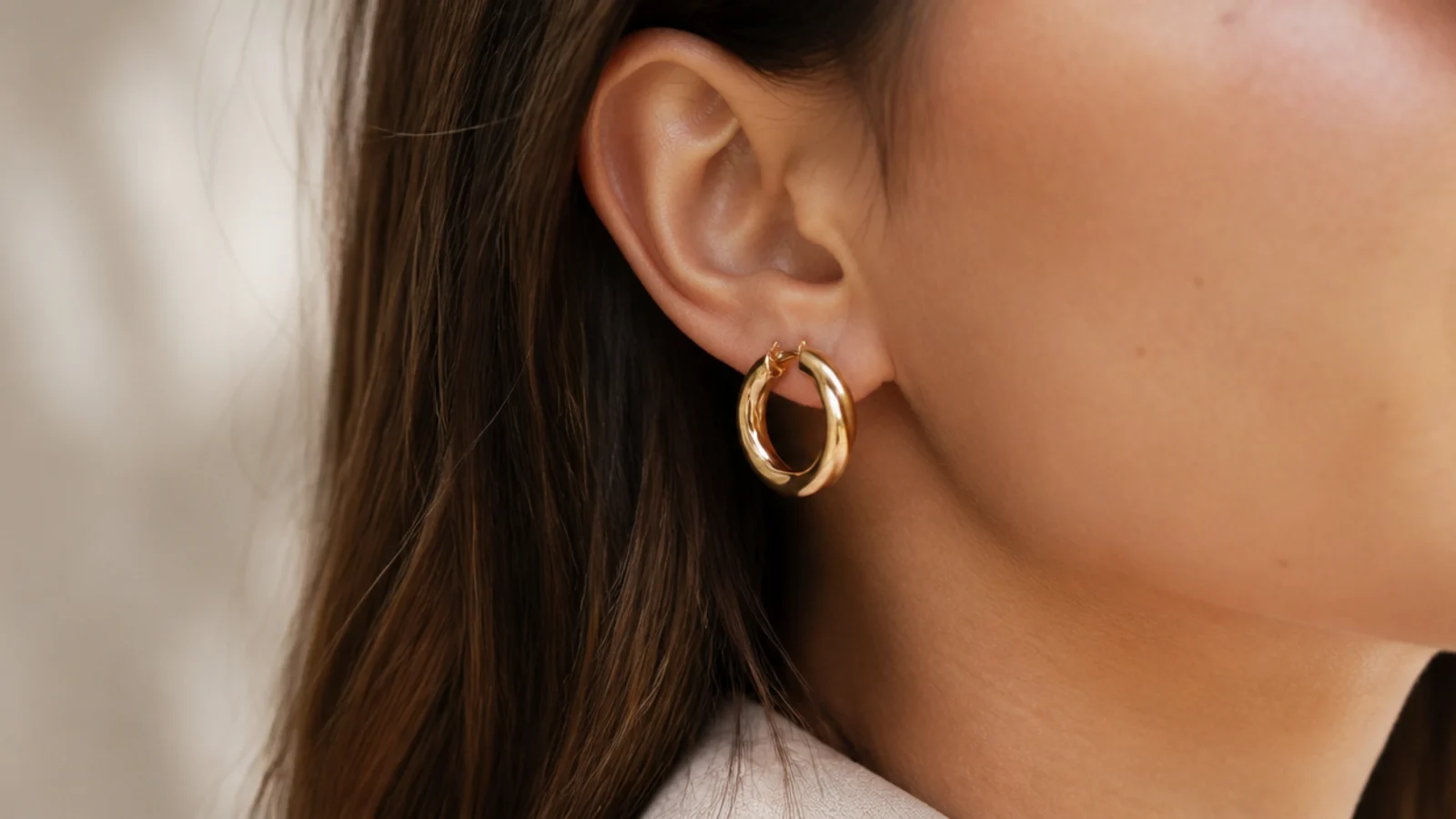Faceless close-up of medium thickness gold hoop earrings about 25 millimeters across