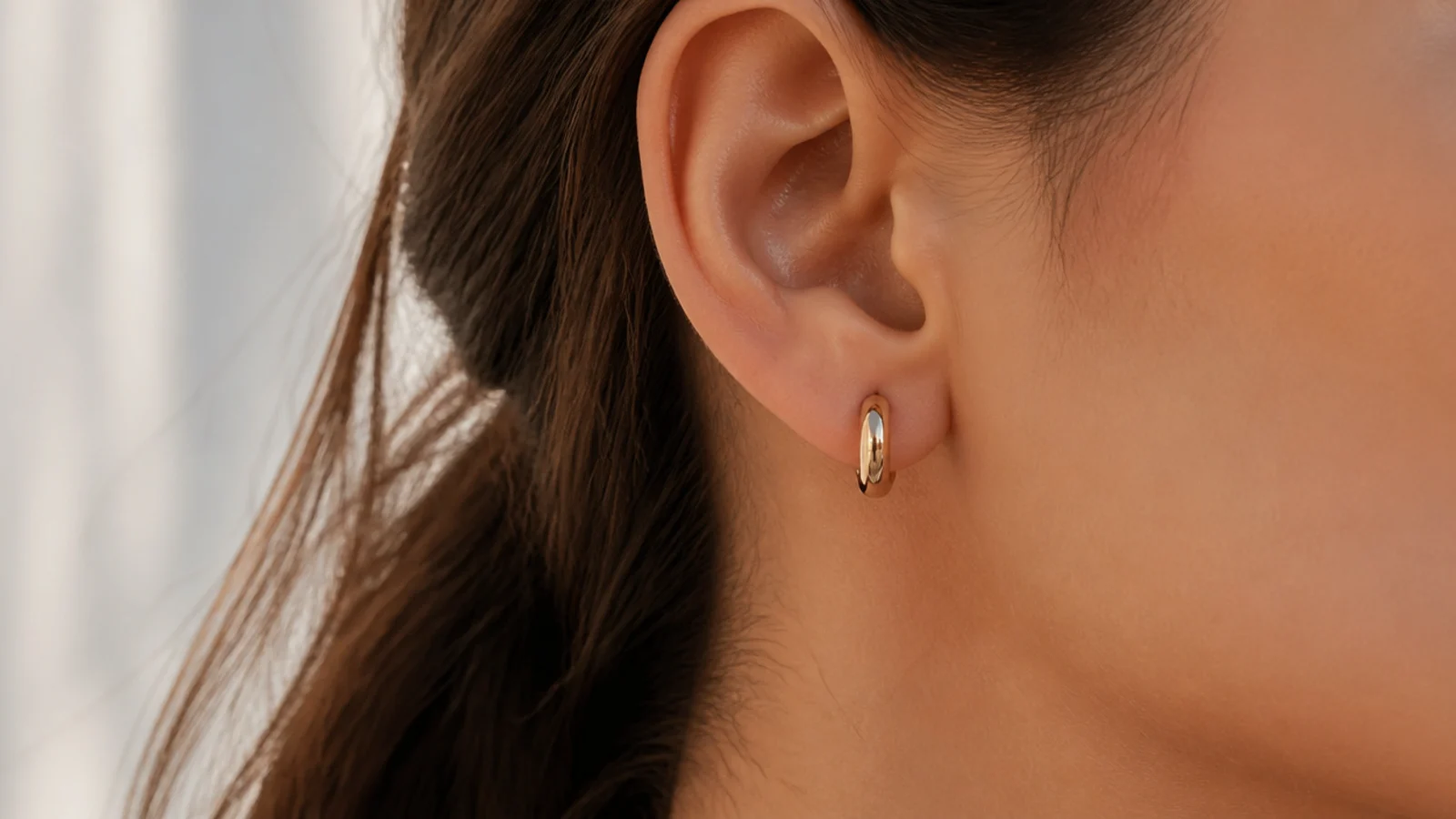 Faceless close-up of small gold huggie hoop earrings hugging the earlobe