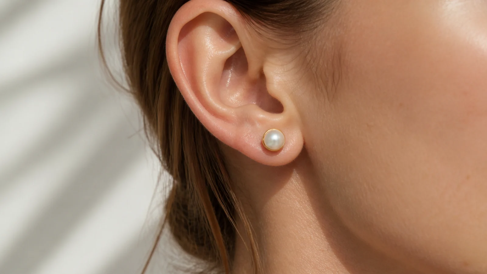 Faceless close-up of a single white freshwater pearl stud earring in a gold cup setting