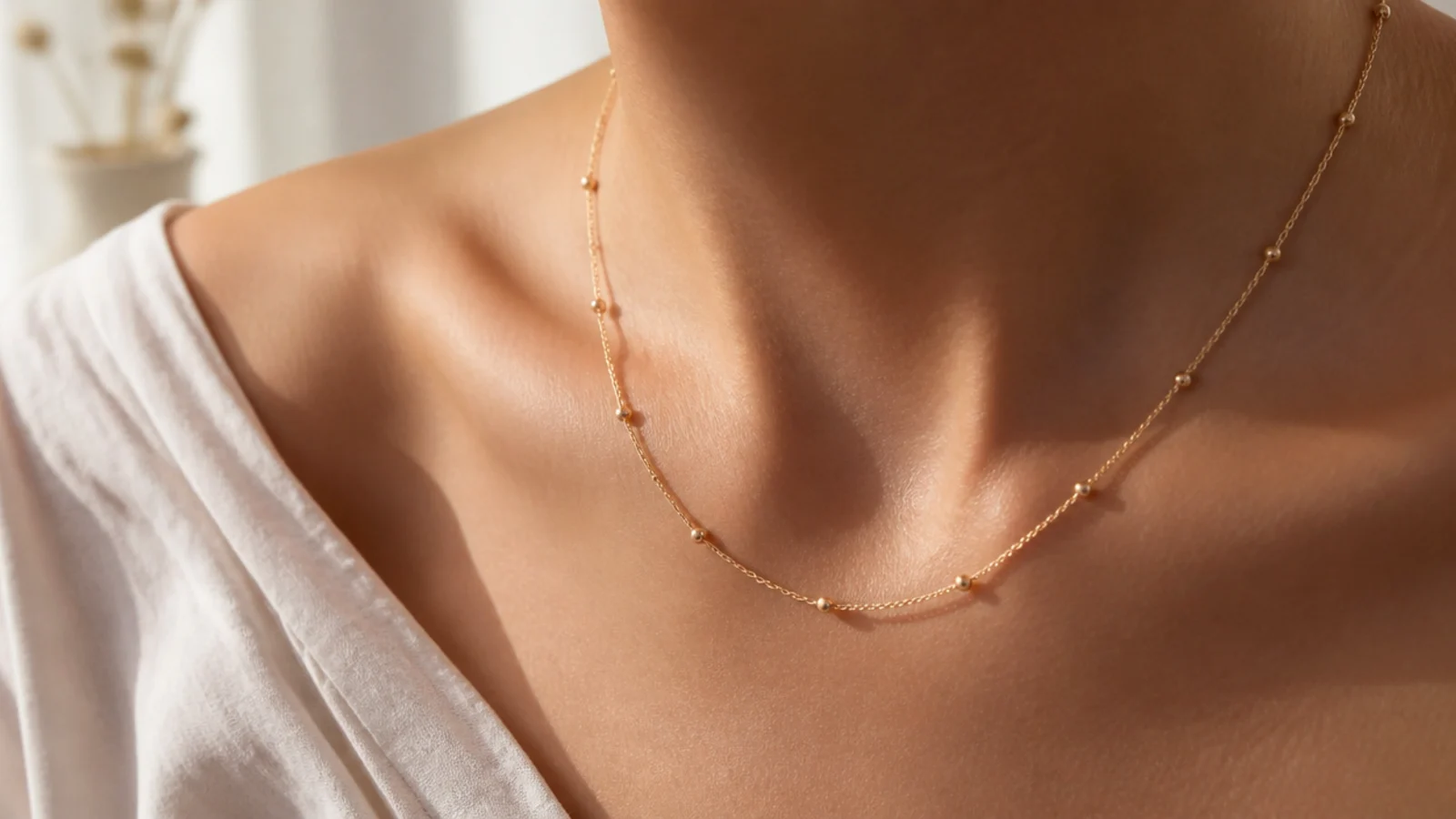 Faceless close-up of a fine gold station necklace with tiny beads spaced along the chain