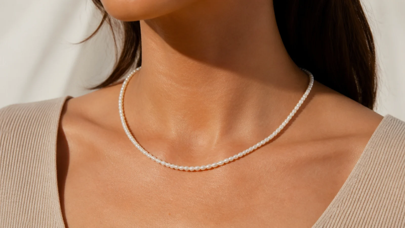 Faceless close-up of a single strand of small white freshwater pearls at princess length