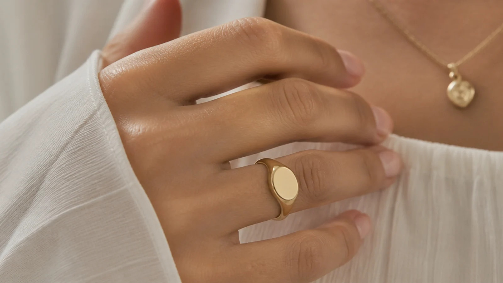 Faceless close-up of a smooth flat-faced gold signet ring worn on the pinky finger