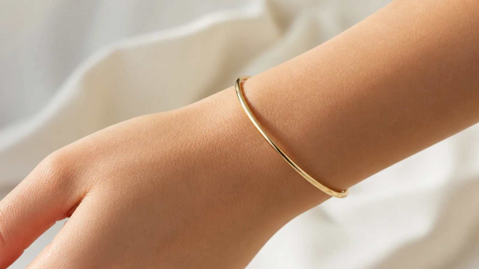 Faceless close-up of a smooth thin round gold bangle bracelet on the wrist