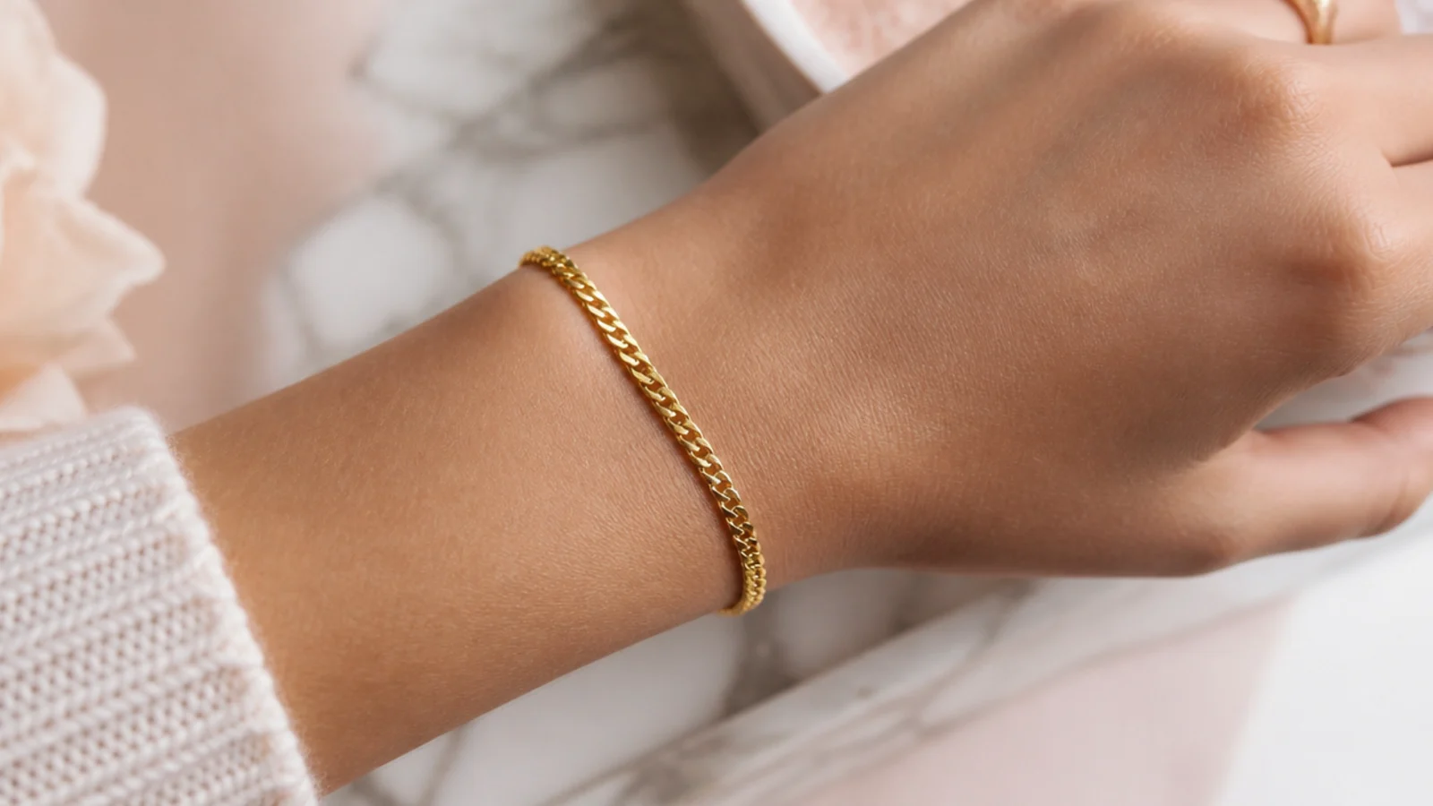 Faceless close-up of a fine gold curb chain bracelet fastened at the wrist