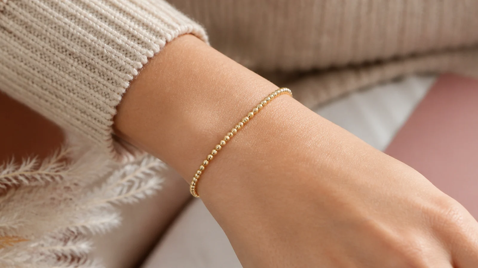 Faceless close-up of a delicate gold beaded bracelet with tiny beads on an elastic cord