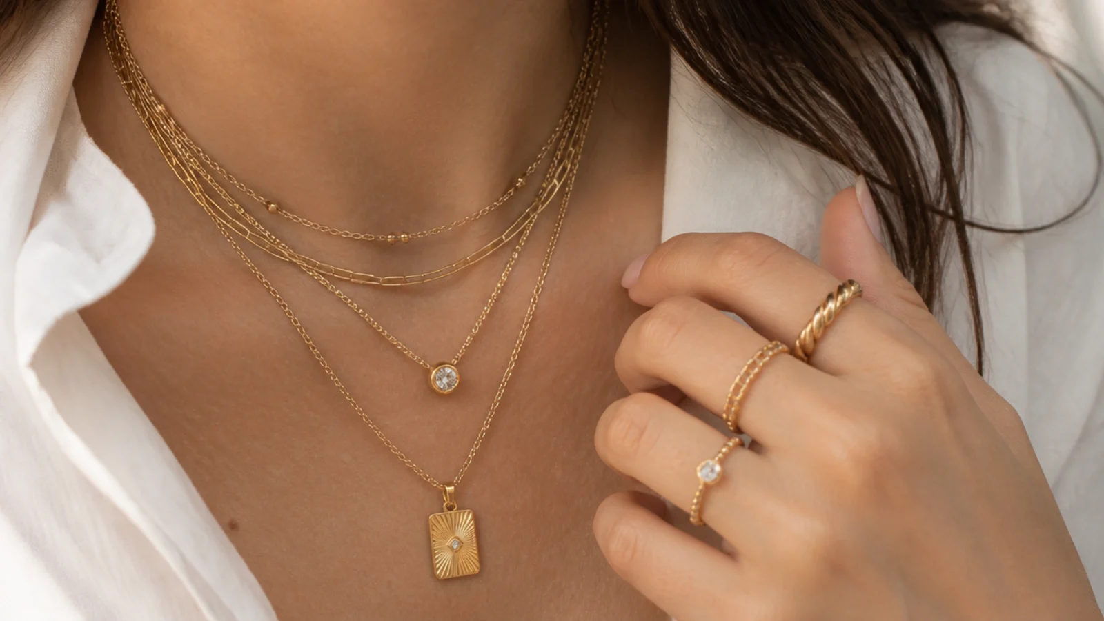 Faceless close-up of layered gold necklaces and stacked rings worn together on one person