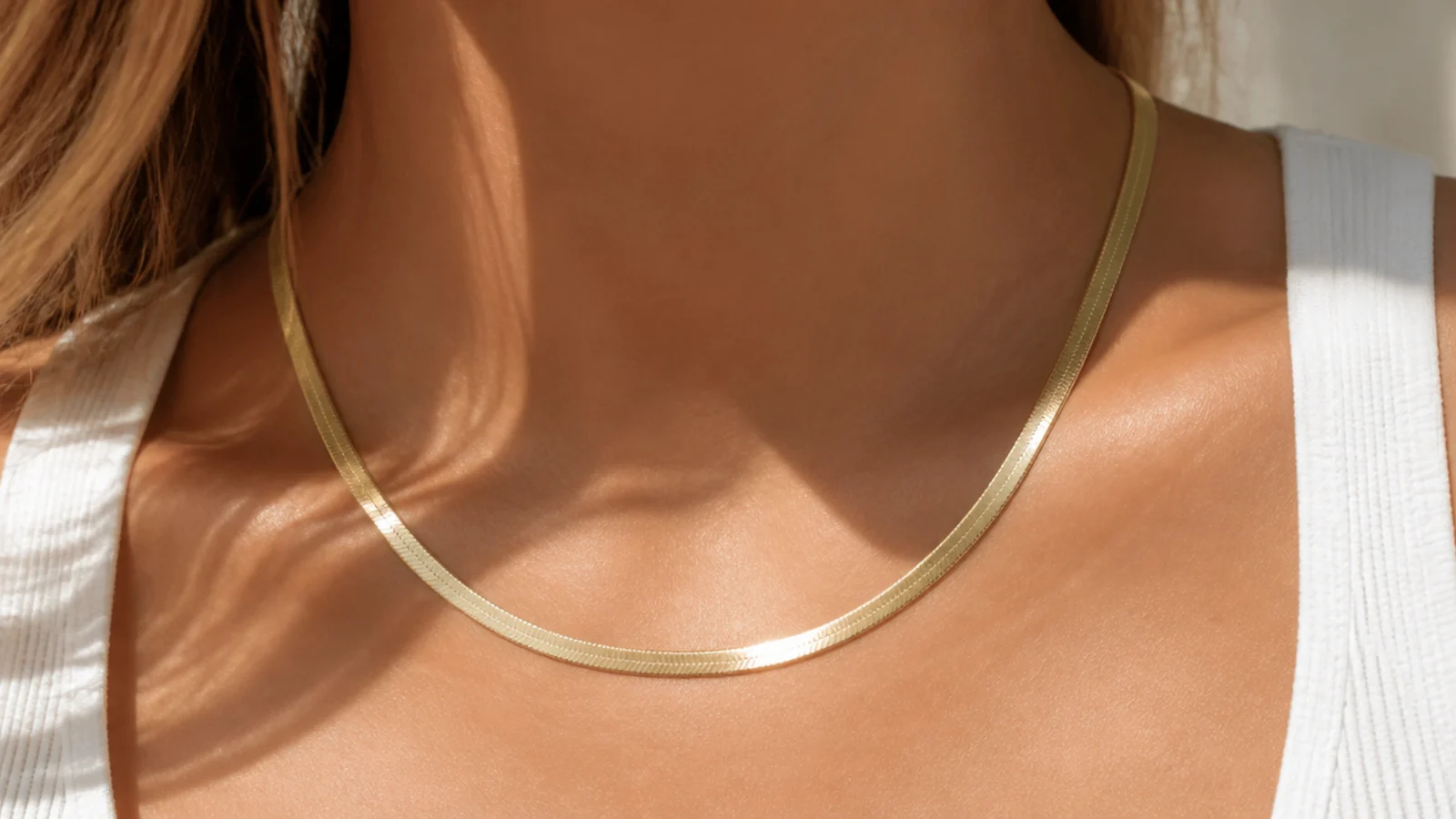 Faceless close-up of a flat gold herringbone chain necklace on warm skin, an affordable statement pick under fifty dollars