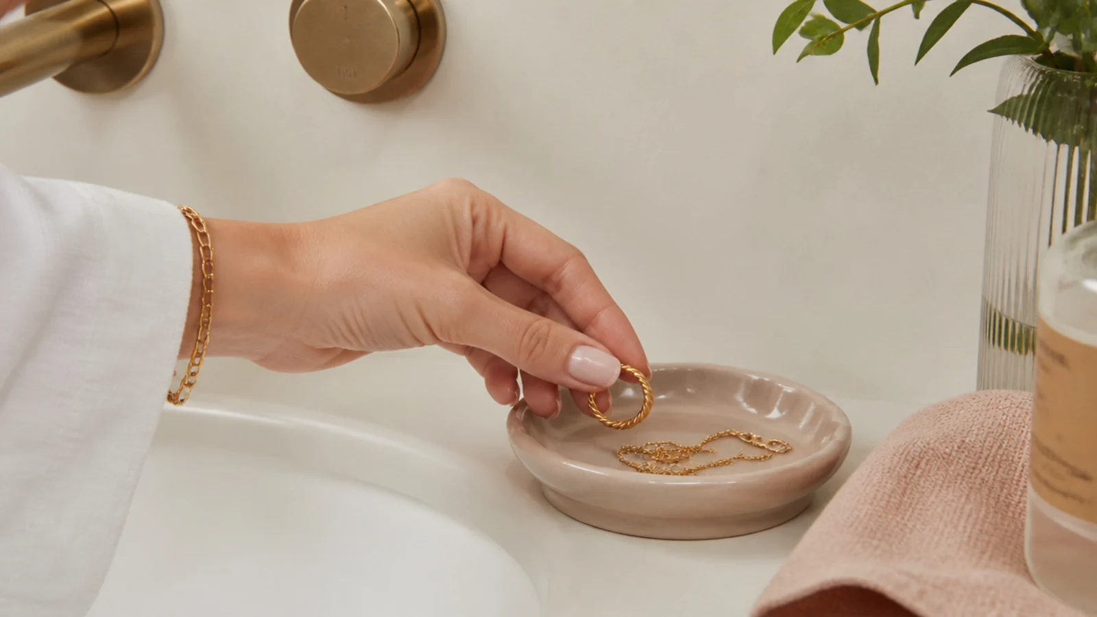 Faceless close-up of a hand setting a gold ring into a dish beside a bathroom sink before showering