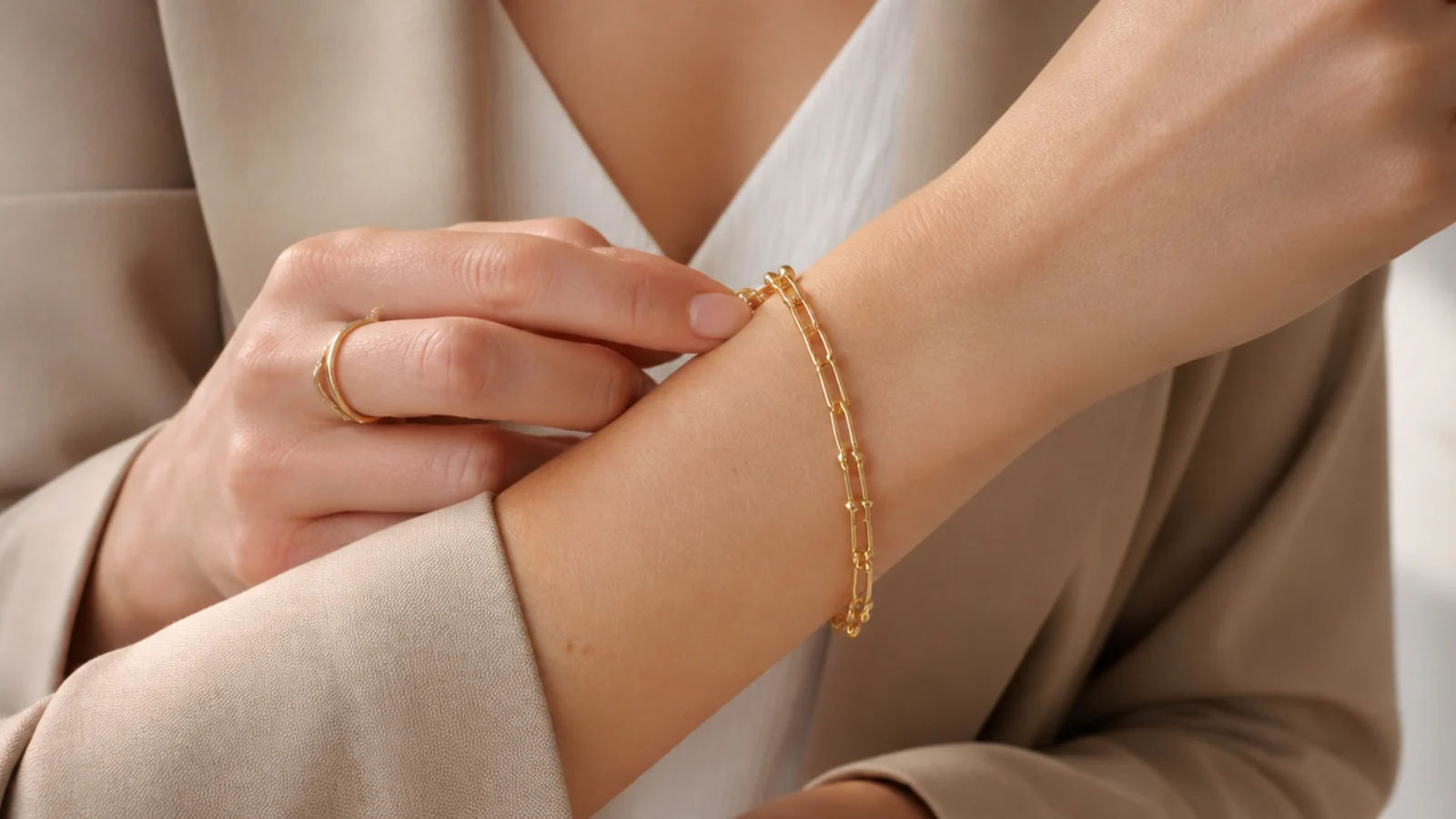 Faceless close-up of a fully dressed wrist fastening a gold chain bracelet as the final step