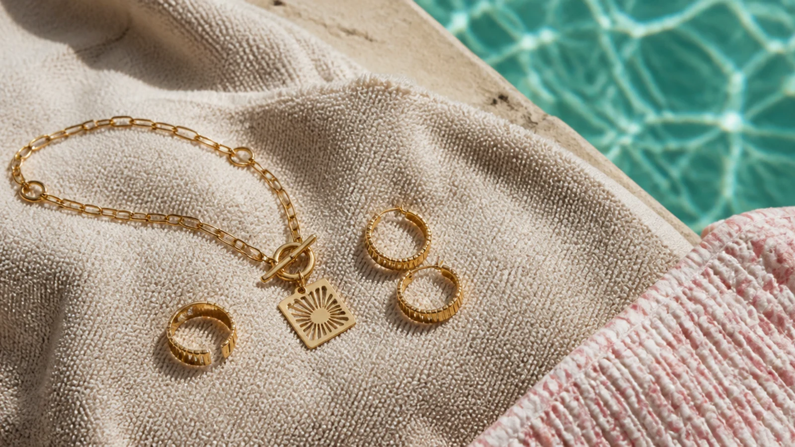 Faceless close-up of gold jewelry set aside on a towel at the edge of a swimming pool