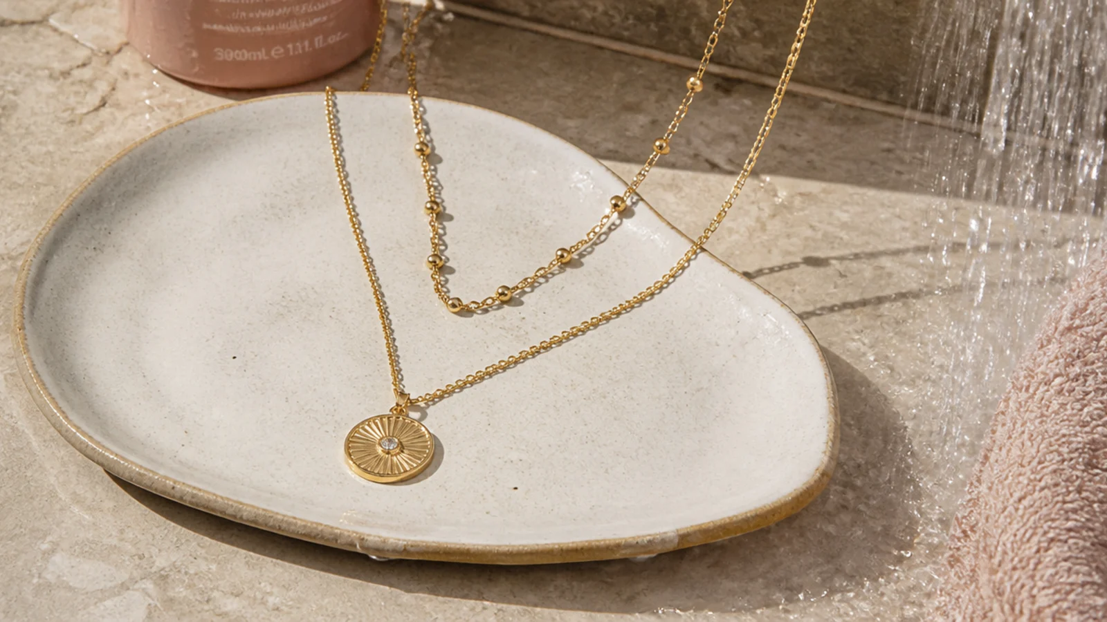 Faceless close-up of a gold-plated necklace set on a dish outside a running shower