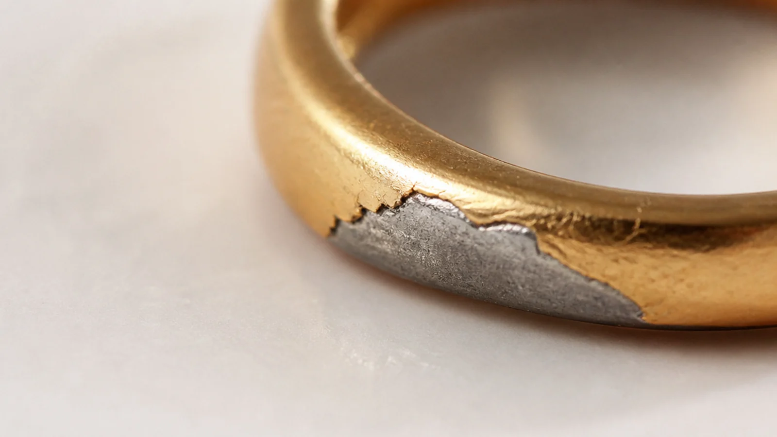 Faceless macro close-up of a gold-plated surface showing the thin gold layer over a base metal core