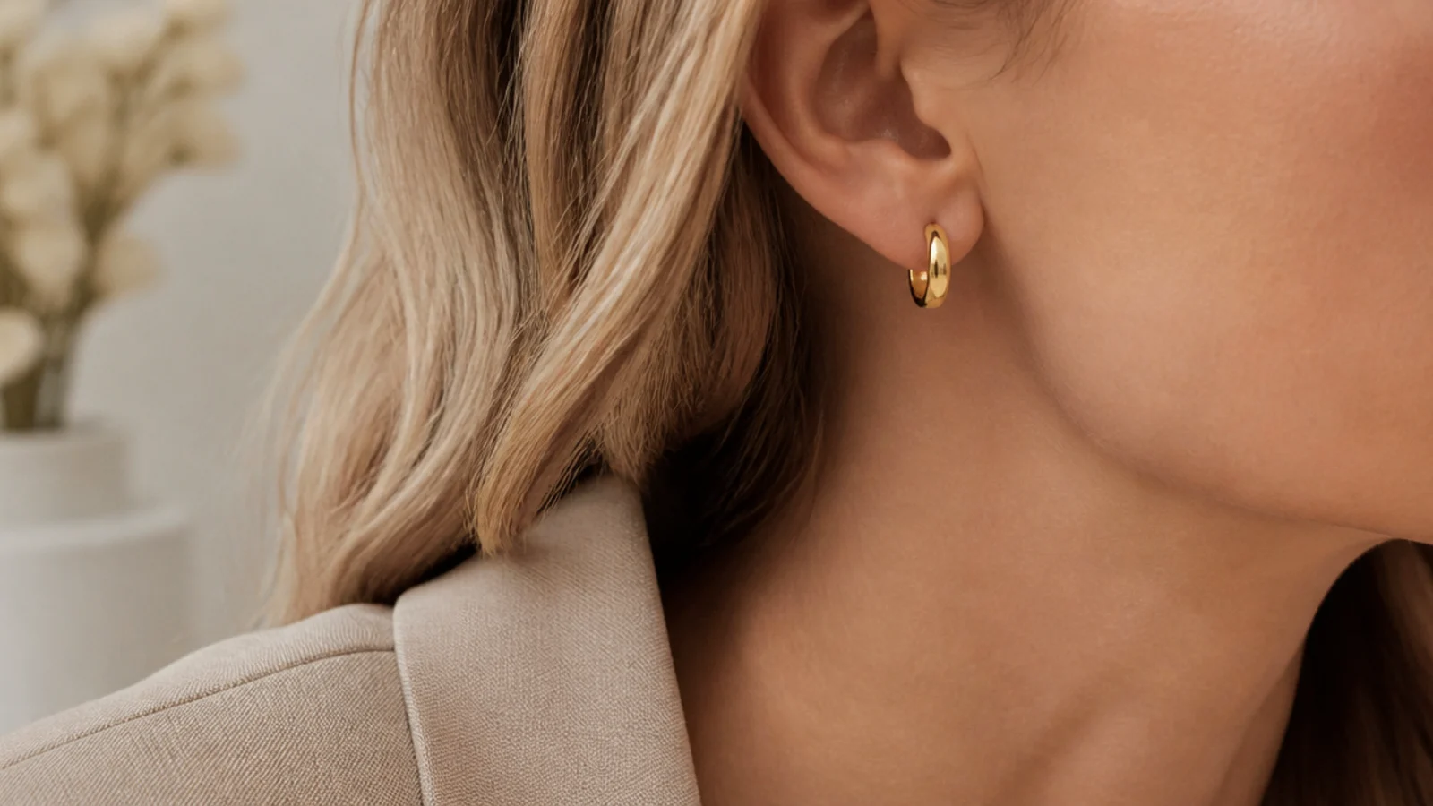 Faceless close-up of small gold huggie hoop earrings worn with a beige blazer for work