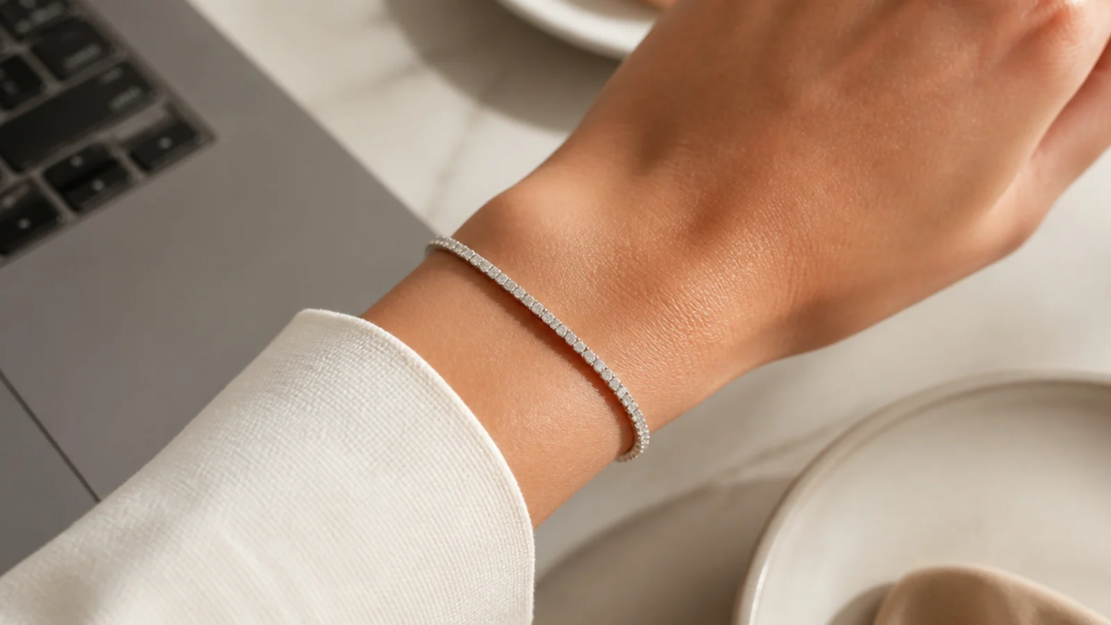 Faceless close-up of a slim diamond tennis bracelet on a wrist beside a blazer cuff at work