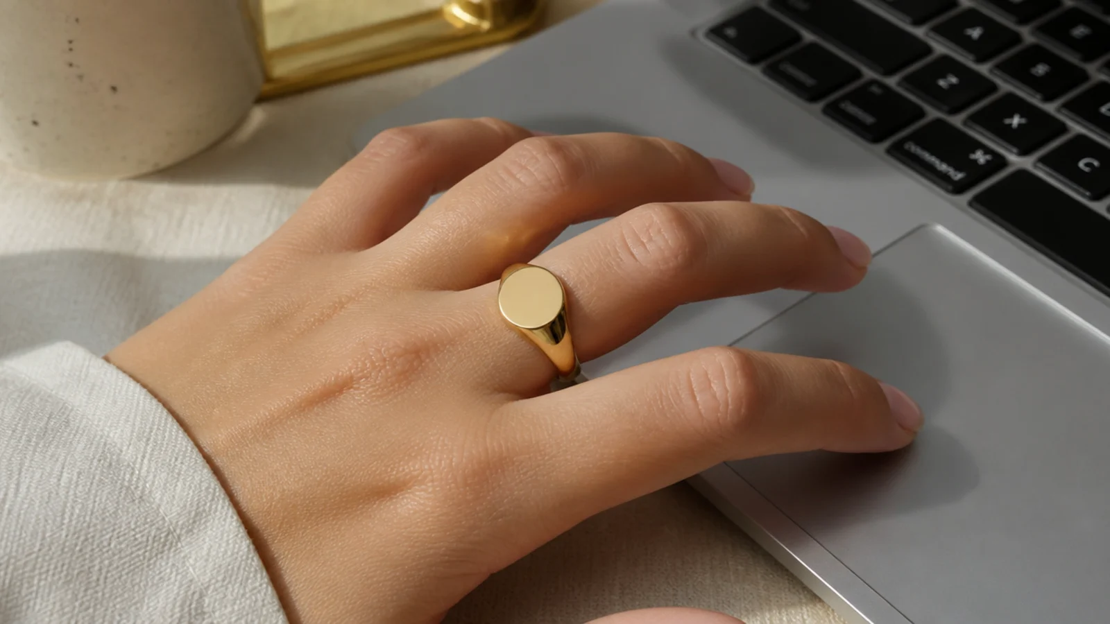 Faceless close-up of a plain gold signet ring on a hand resting near a laptop at work