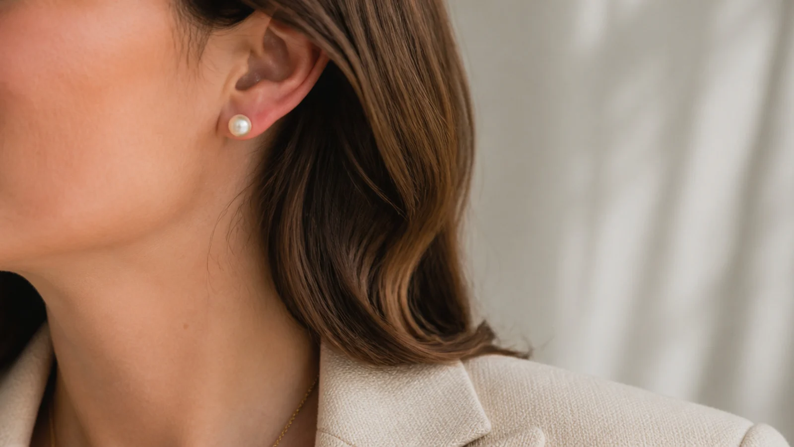 Faceless close-up of classic white pearl stud earrings worn with a structured jacket for an interview