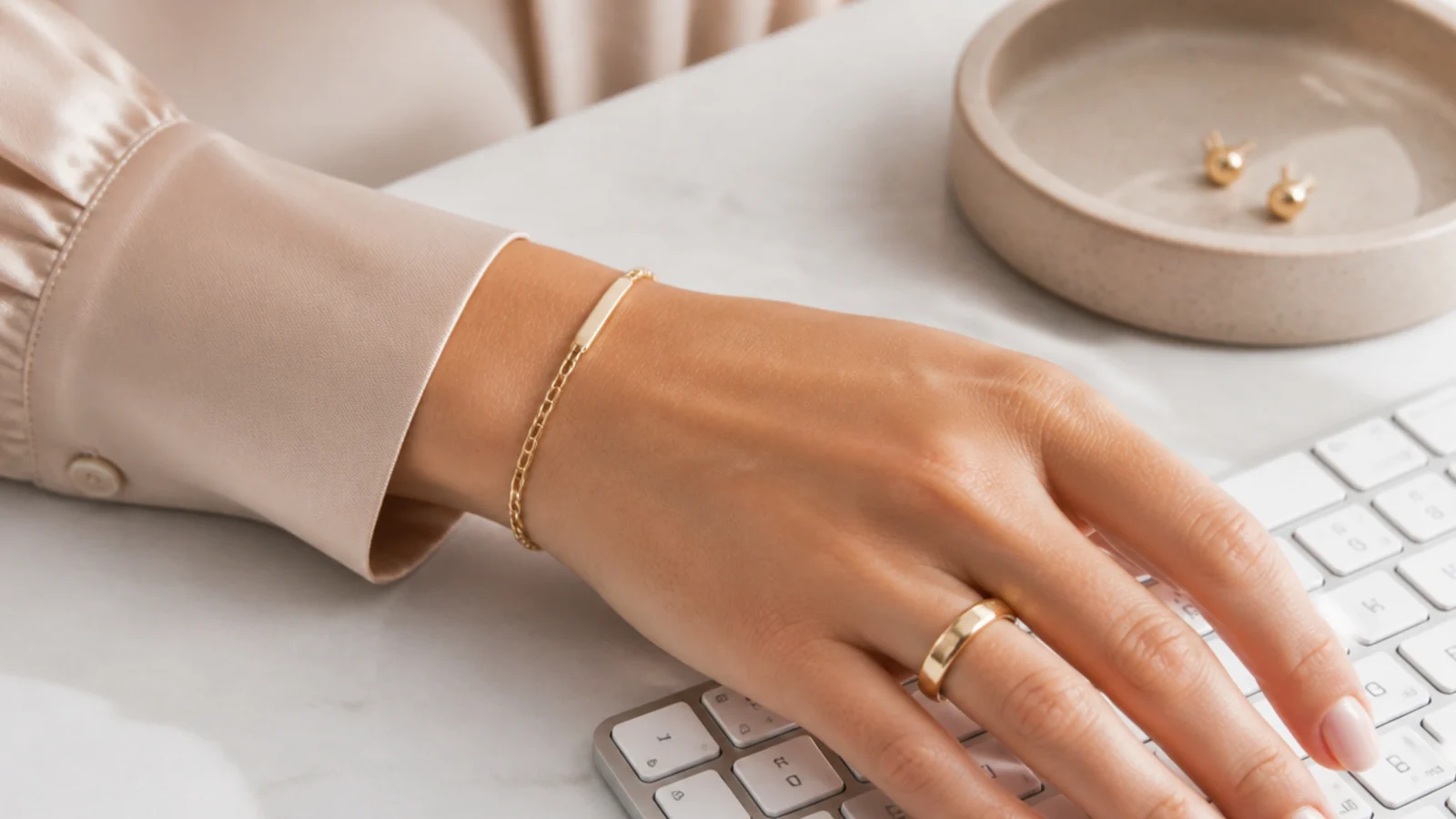 Faceless close-up of low-profile work jewelry on hands, a plain band and stud earrings, near a keyboard