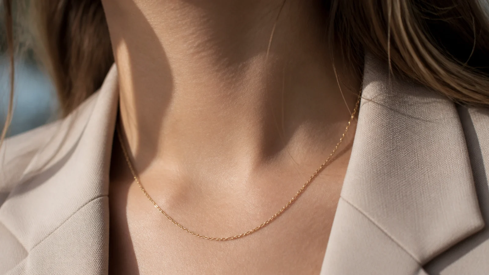 Faceless close-up of minimal interview jewelry, small studs and one thin chain over a jacket