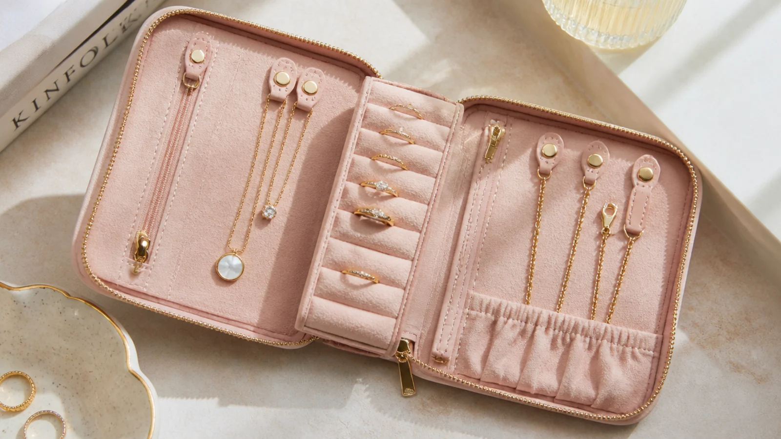 Faceless overhead shot of an open fold-and-roll travel jewelry case with a ring bar, zip pockets and necklace clasps