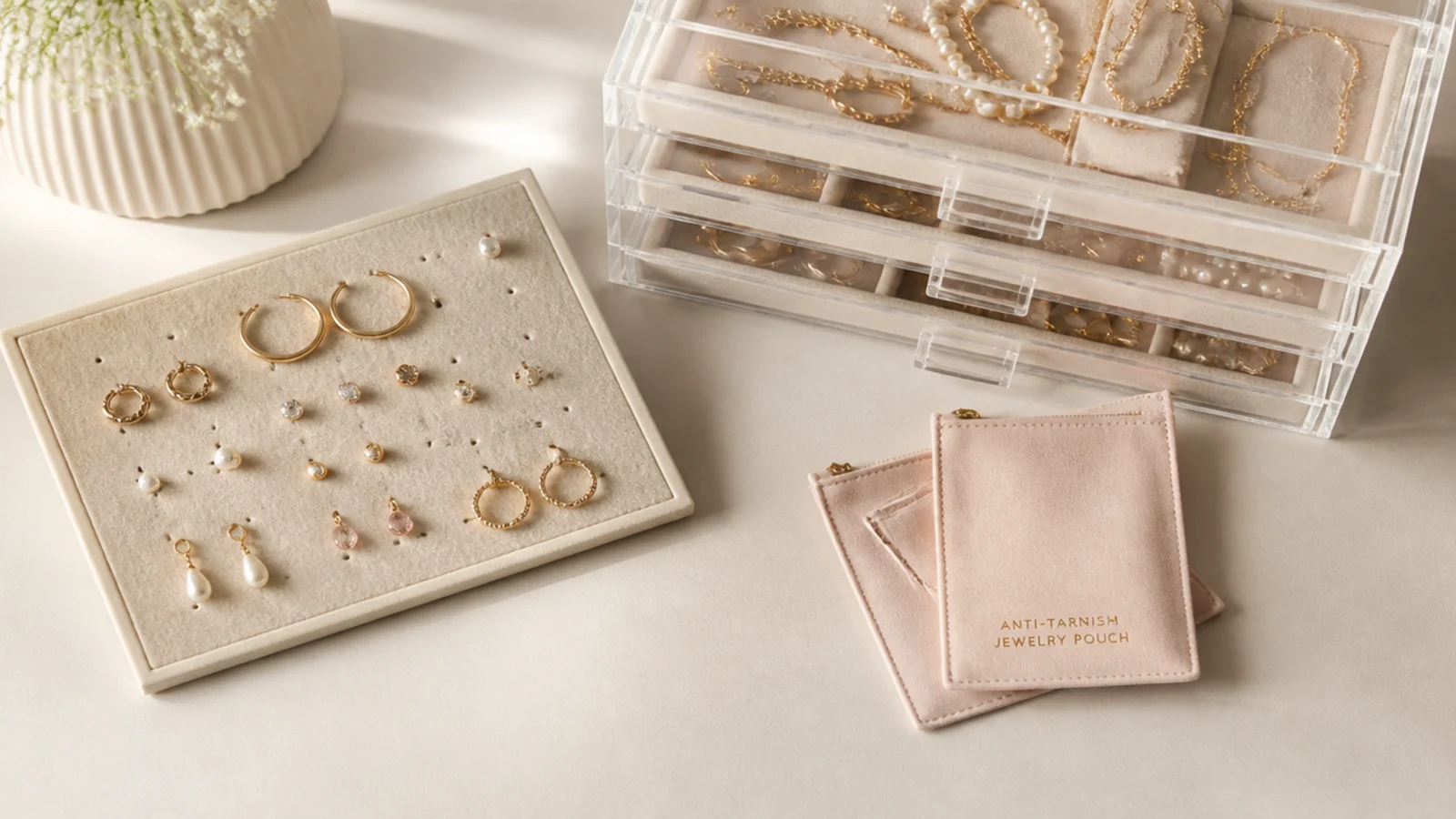 Faceless overhead shot of small-space jewelry organization with a stacked acrylic drawer, earring board and anti-tarnish pouches