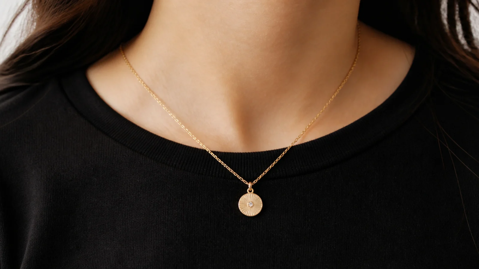 Faceless close-up of a 16-inch gold pendant necklace resting on a black crew-neck cotton top