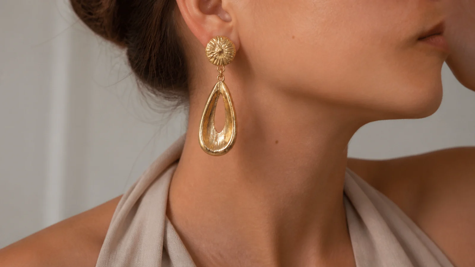 Faceless close-up of gold statement drop earrings worn with a halter neckline and bare collarbone