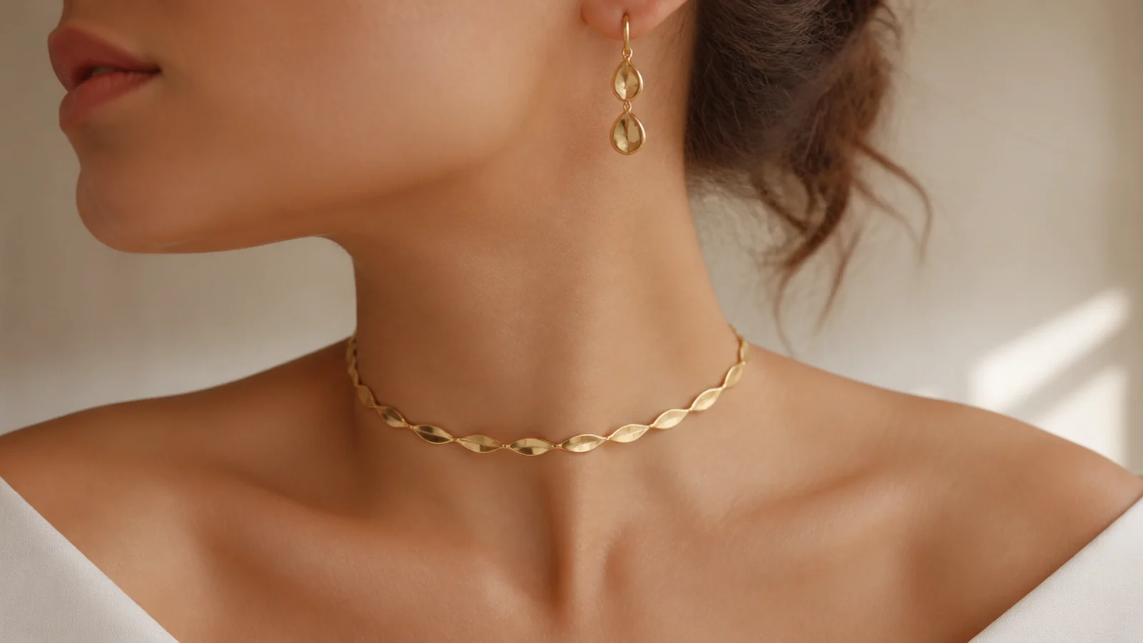 Faceless close-up of a gold choker and drop earrings styled with a bare off-shoulder neckline
