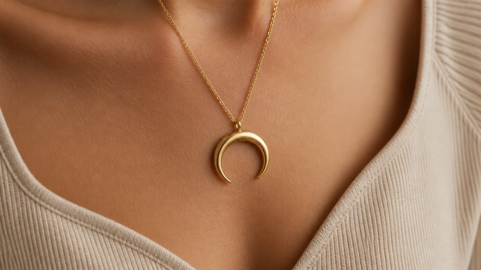 Faceless close-up of a curved crescent gold pendant following a sweetheart neckline