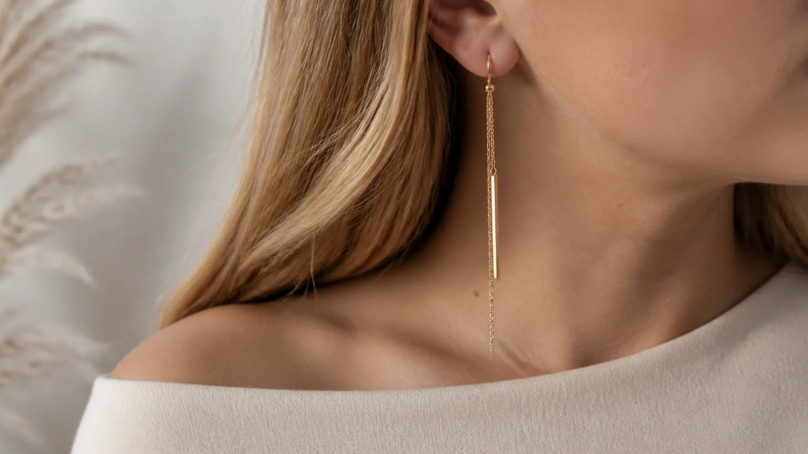 Faceless close-up of long gold drop earrings worn with a wide boat neckline