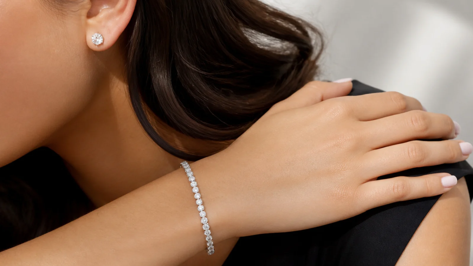 Faceless close-up of diamond stud earrings and a tennis bracelet styled with a simple black dress