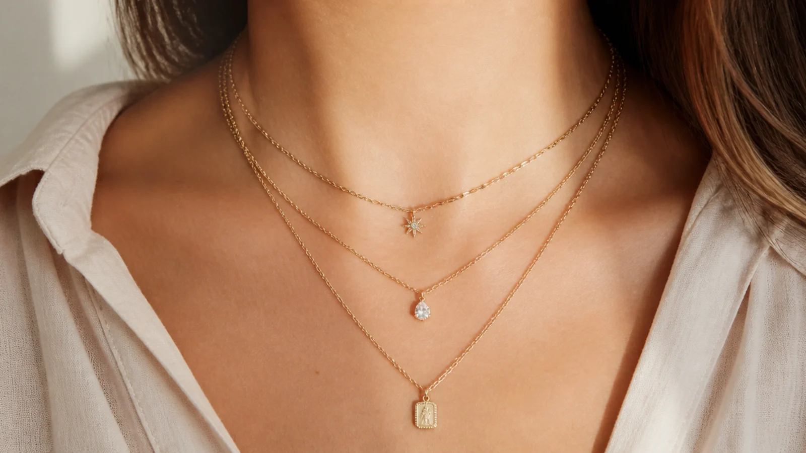 Faceless close-up of three gold necklaces layered at staggered lengths showing clear spacing between each chain