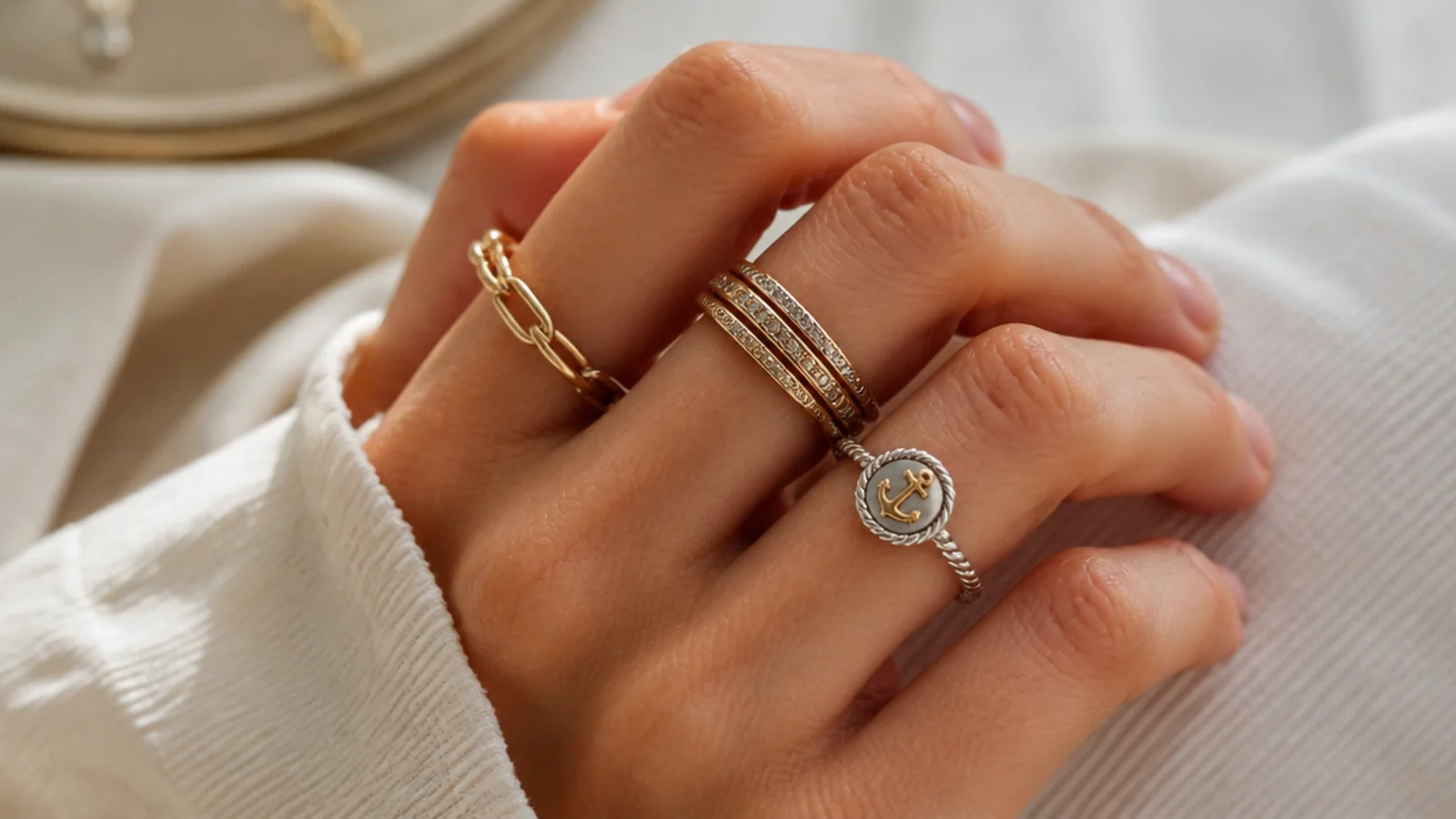 Faceless close-up of stacked gold and silver rings mixed on one hand with a two-tone anchor ring