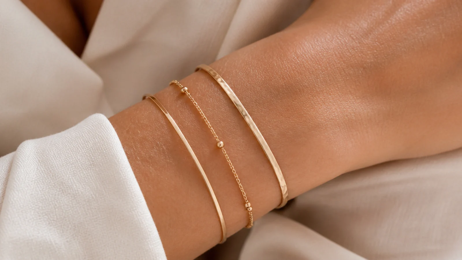 Faceless close-up of a stacked wrist wearing a thin bangle, a fine chain bracelet and a slim cuff