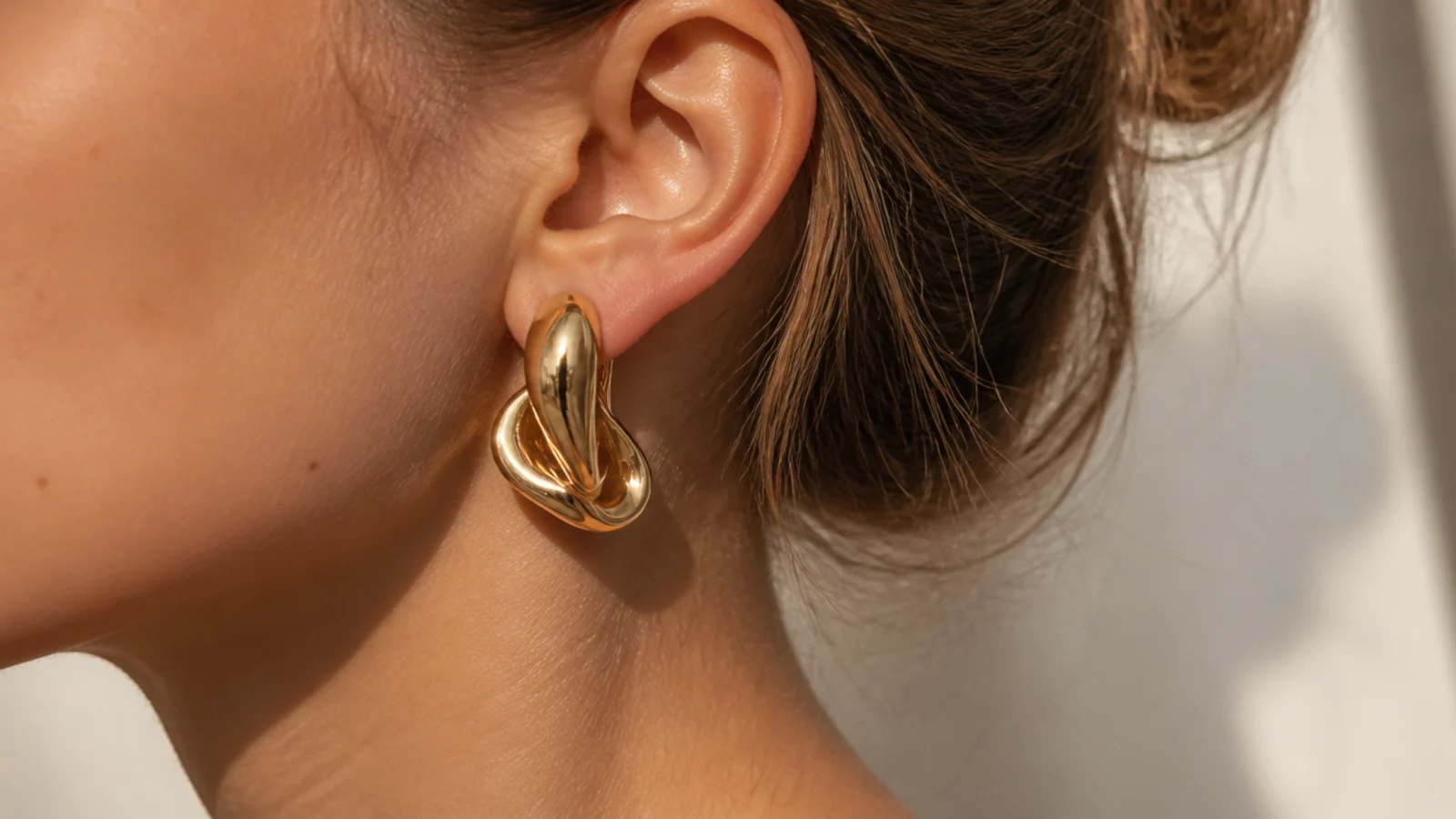 Faceless close-up of one bold sculptural gold earring with a clean bare neckline and no necklace