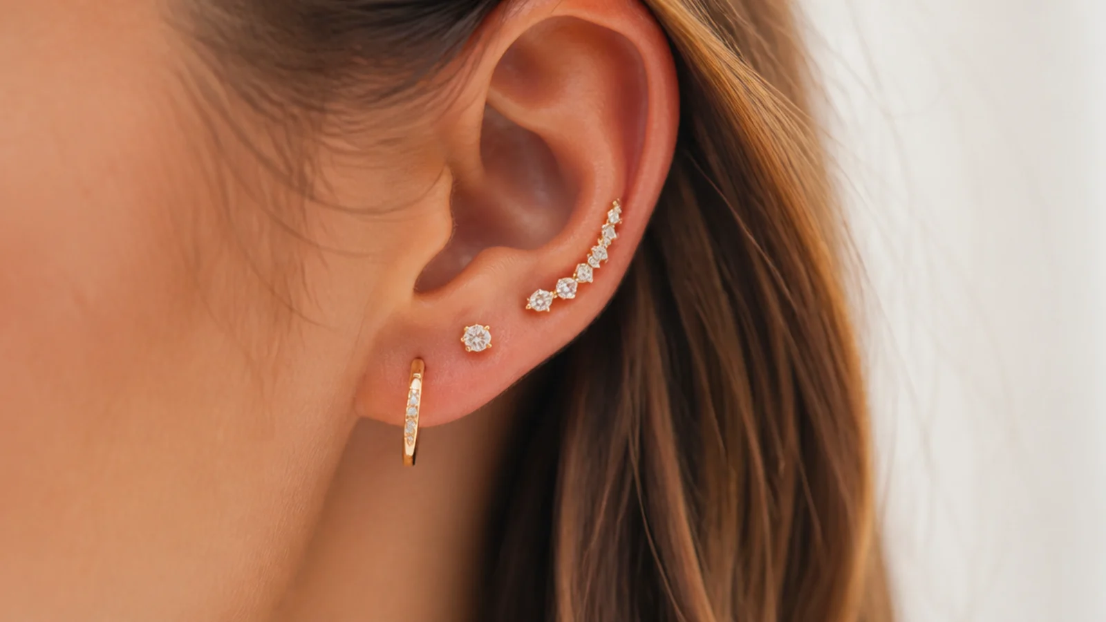 Faceless close-up of a curated ear stack with a stud, a small huggie hoop and an ear climber