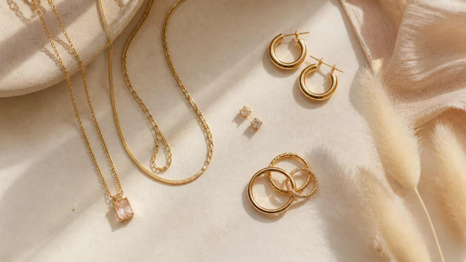 Faceless flat-lay of a compact jewelry set with studs, hoops, a pendant, layering chains and stacking rings