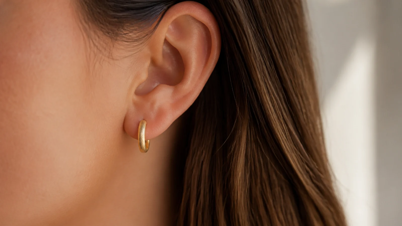 Faceless close-up of a small brushed gold huggie hoop hugging the earlobe