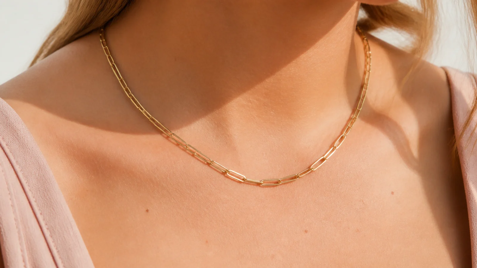 Faceless close-up of a fine gold paperclip-link chain necklace resting at the collarbone