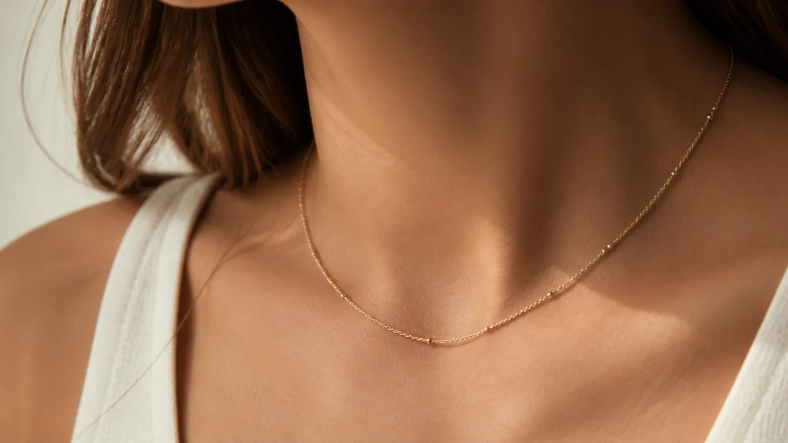 Faceless close-up of a delicate gold satellite chain with tiny evenly spaced beads at the neckline