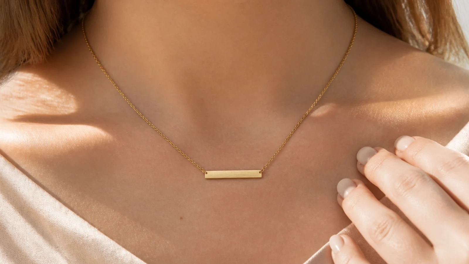 Faceless close-up of a slim horizontal brushed gold bar pendant on a fine chain