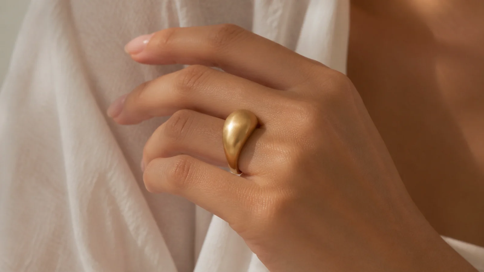 Faceless close-up of a smooth brushed gold dome ring worn alone on a finger