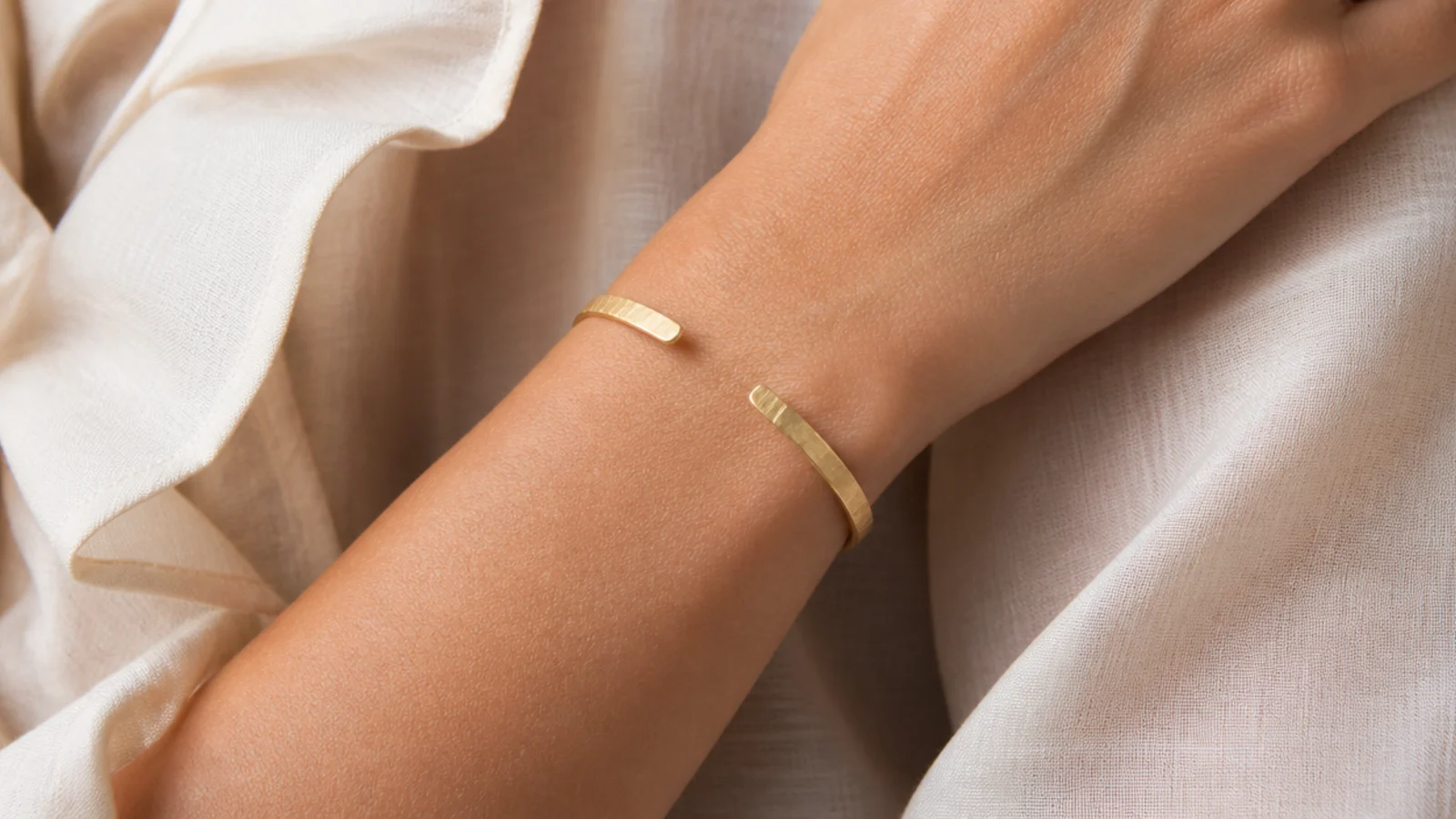 Faceless close-up of a slim open brushed gold cuff bracelet on a wrist