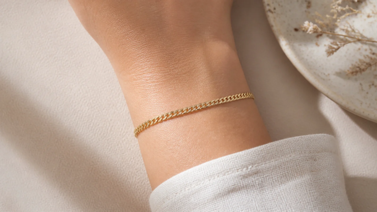 Faceless close-up of a dainty flat gold curb chain bracelet draped on a wrist