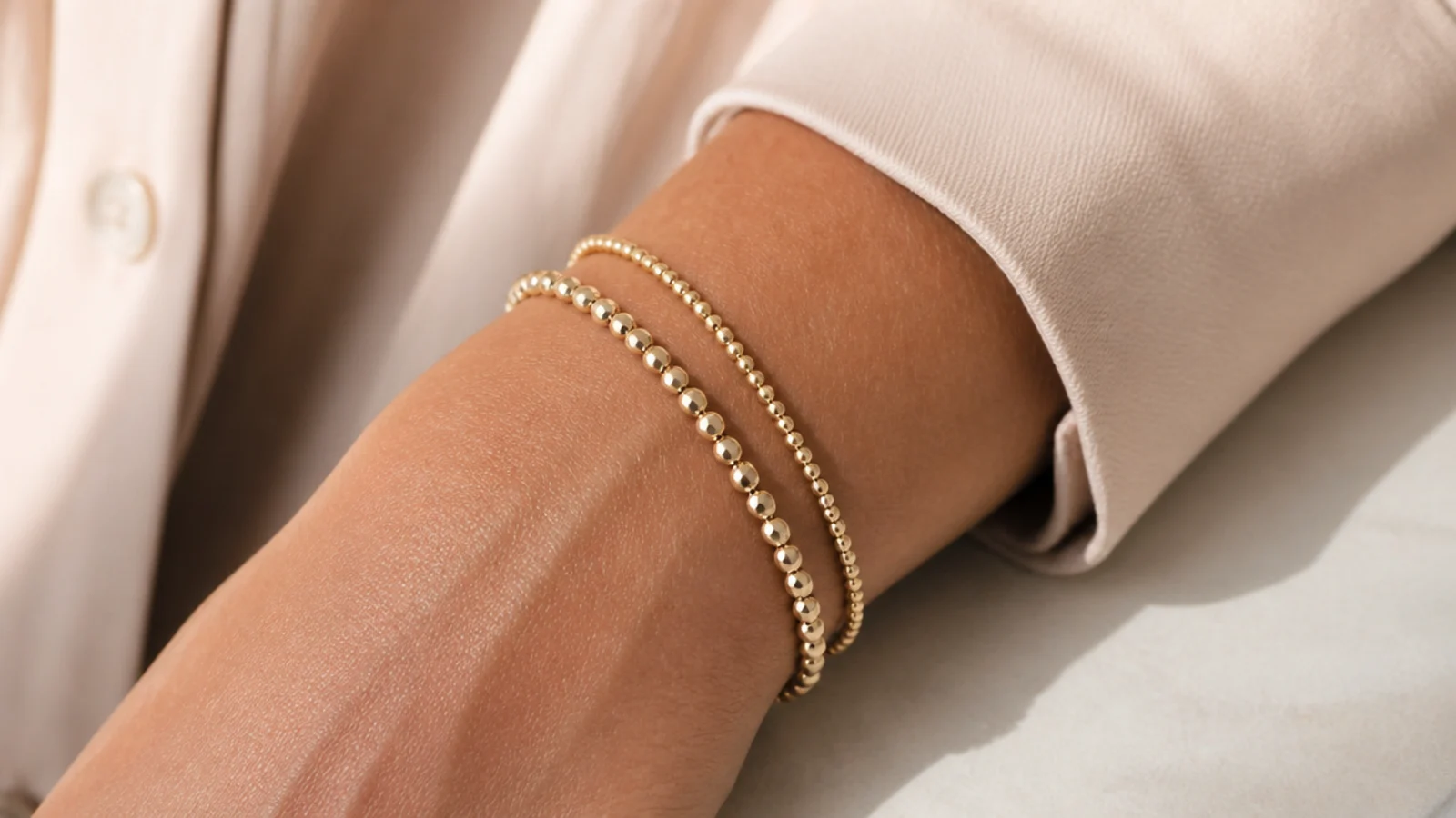 Faceless close-up of two dainty gold beaded bracelets stacked on a wrist