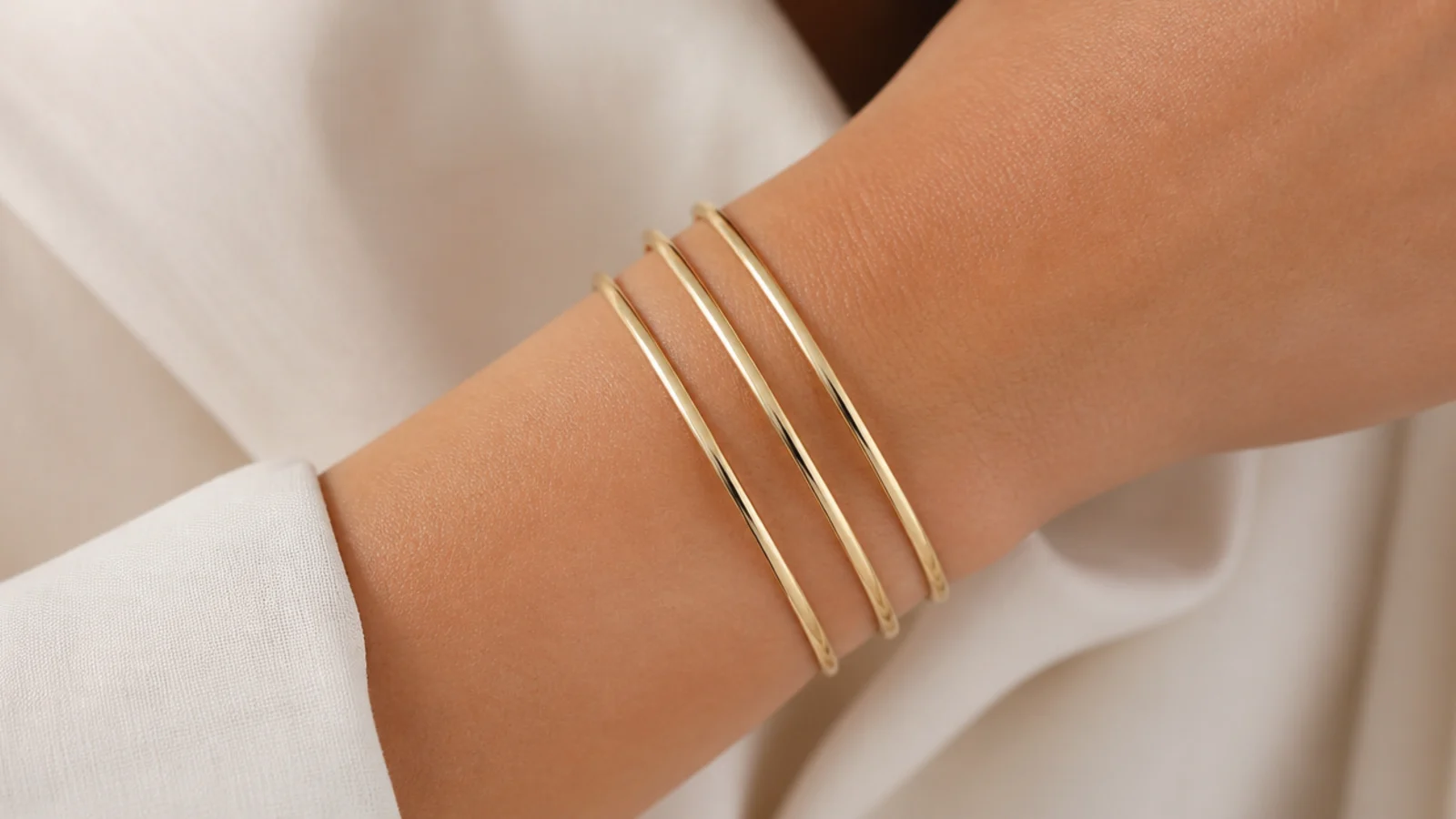 Faceless close-up of three thin smooth gold bangles stacked together on a wrist