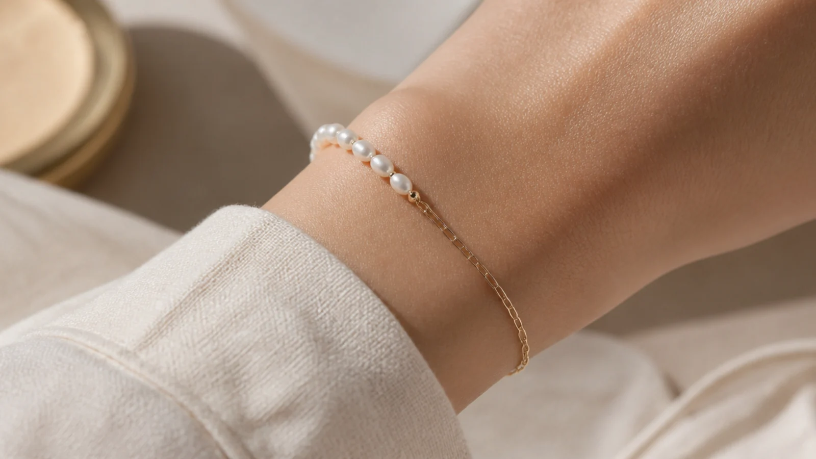 Faceless close-up of a dainty bracelet mixing small freshwater pearls with a fine gold chain on a wrist