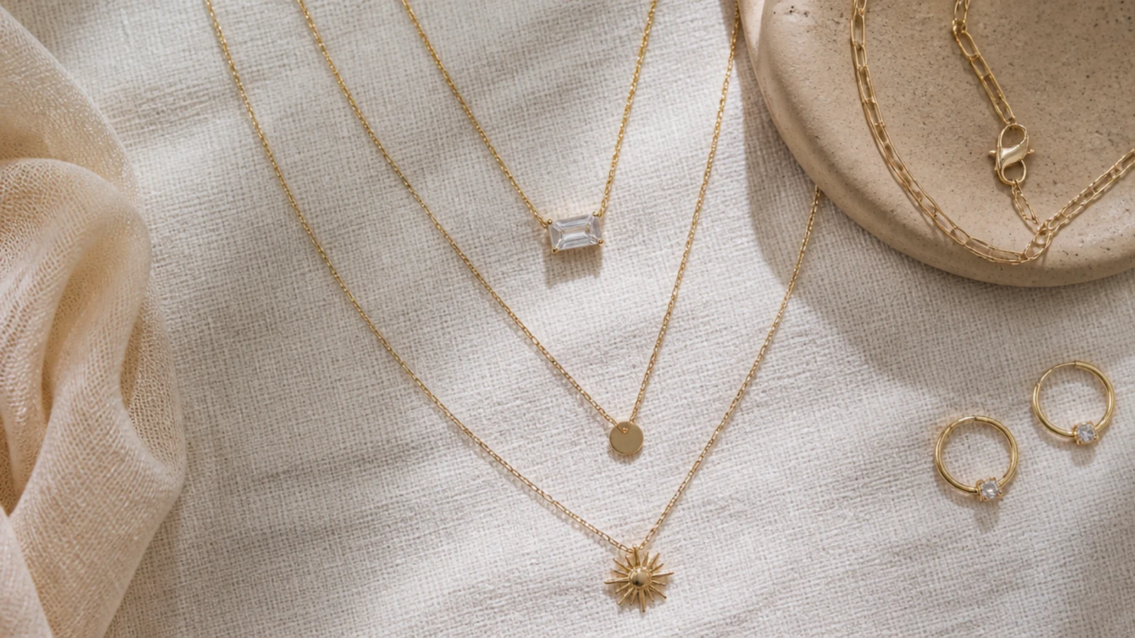 Faceless flat-lay of dainty layered gold pieces styled together on a neutral linen background