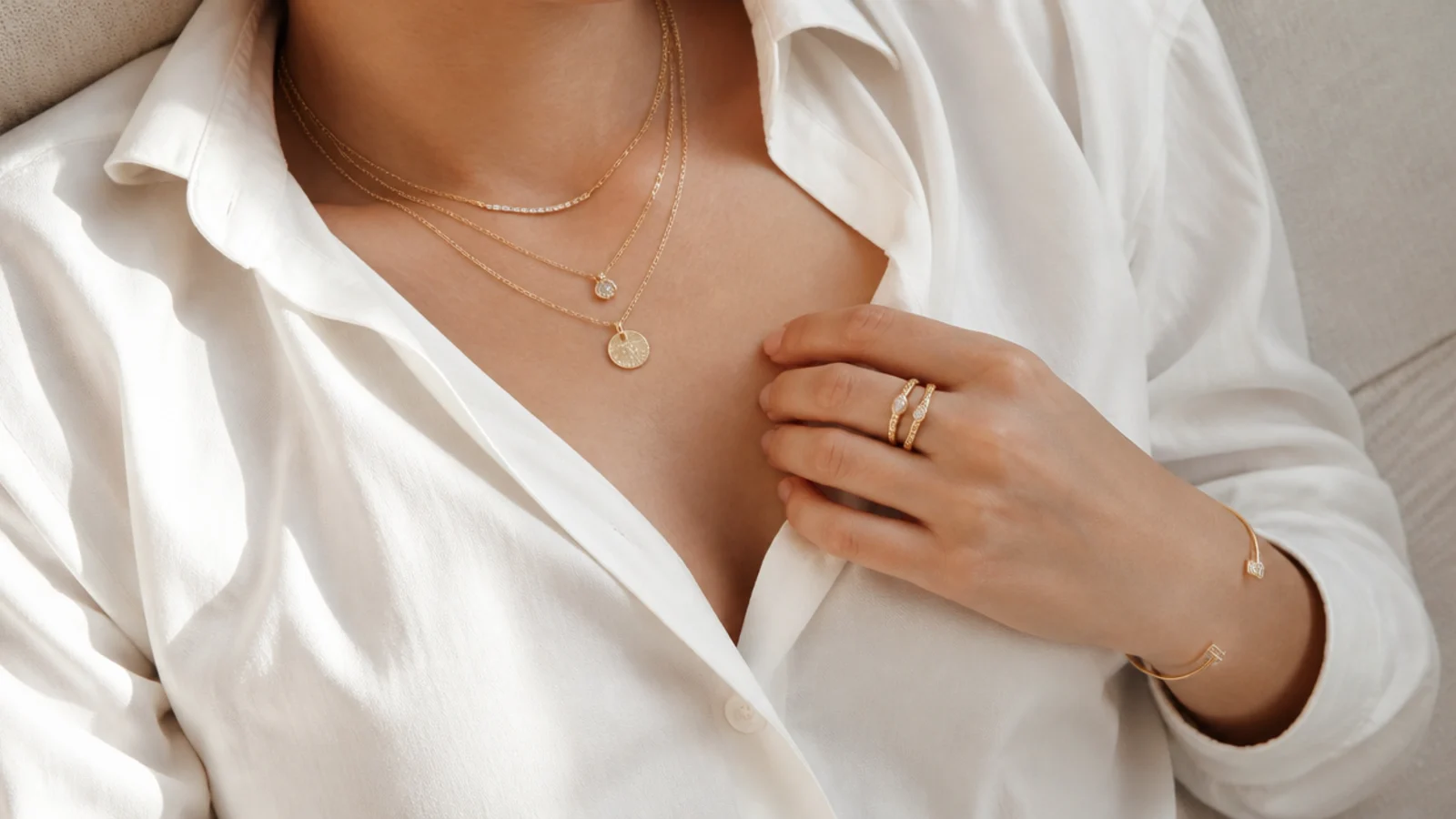 Faceless waist-up flat-lay of layered dainty necklaces, stacked rings and a cuff styled on plain clothing
