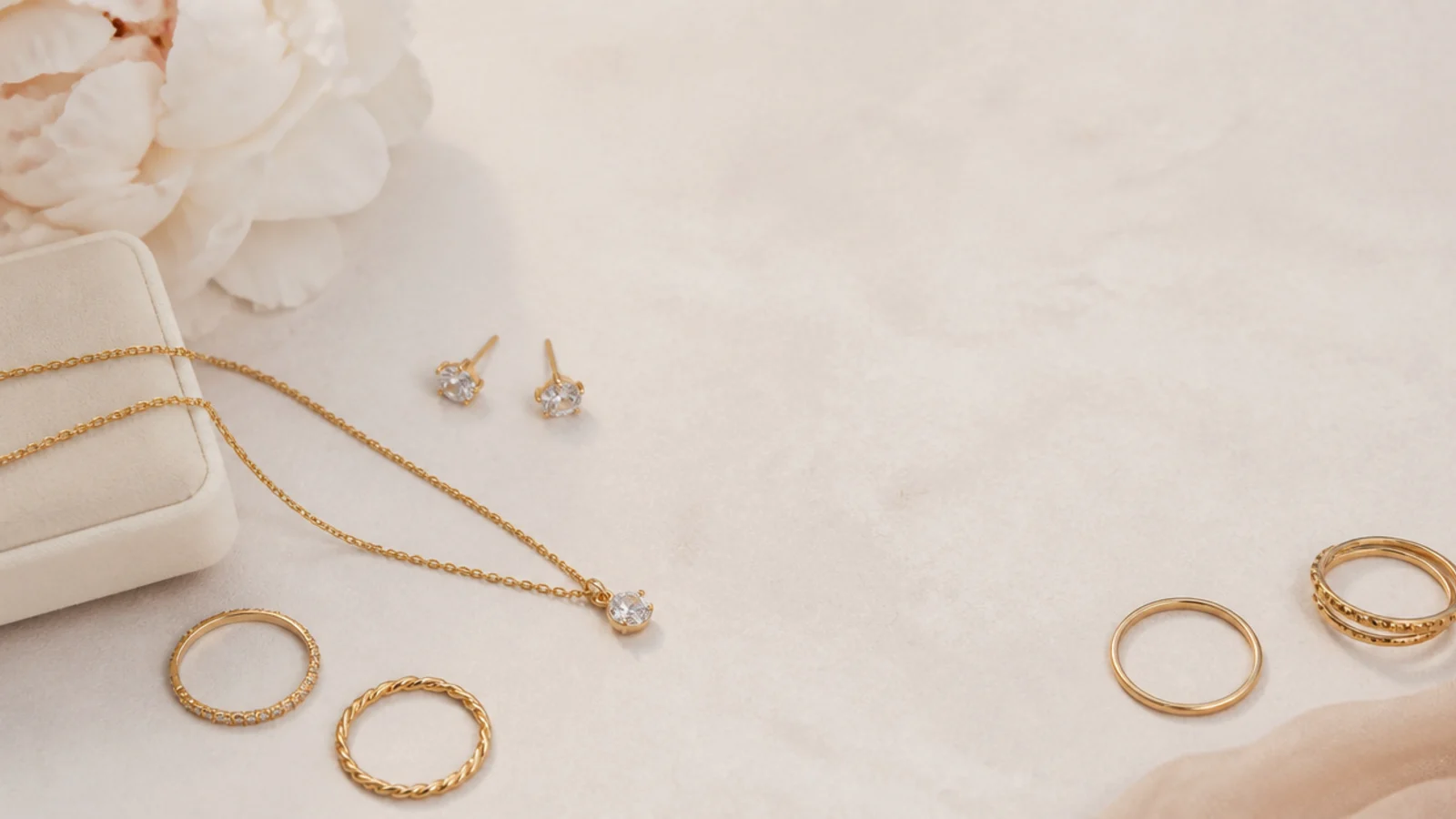 Faceless flat-lay of dainty gold jewelry that looks expensive, with studs, thin chains and stacking rings