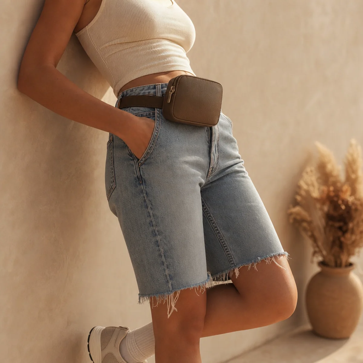 Faceless waist-down shot of denim jorts with a fitted tank, belt bag and sneakers for a festival